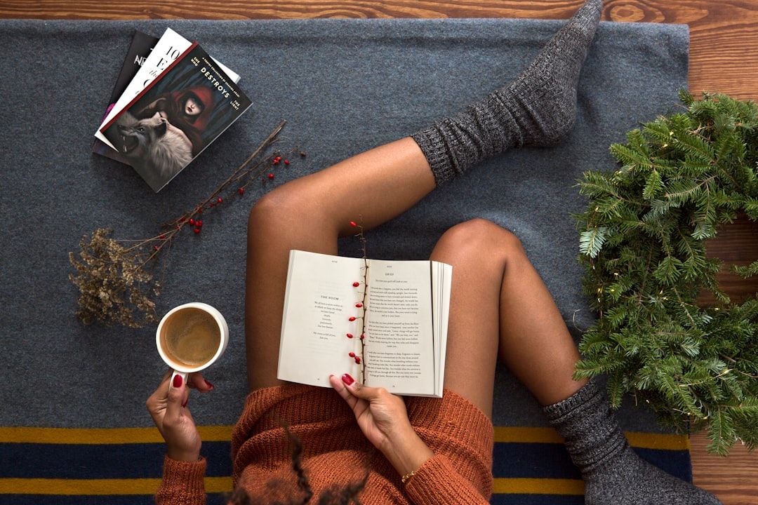 Open book on a reader's lap with a warm drink nearby